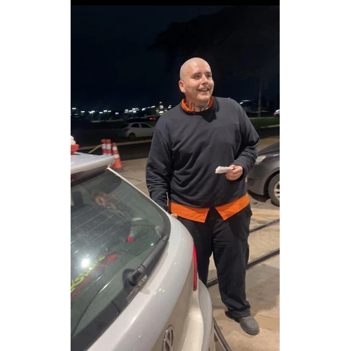 Figurinha: Homem careca sorrindo com camisa laranja